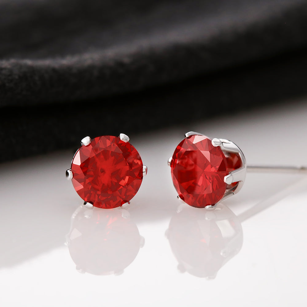 A pair of red cubic zirconia stud earrings with 14K white gold dipped settings, displayed against a reflective background.